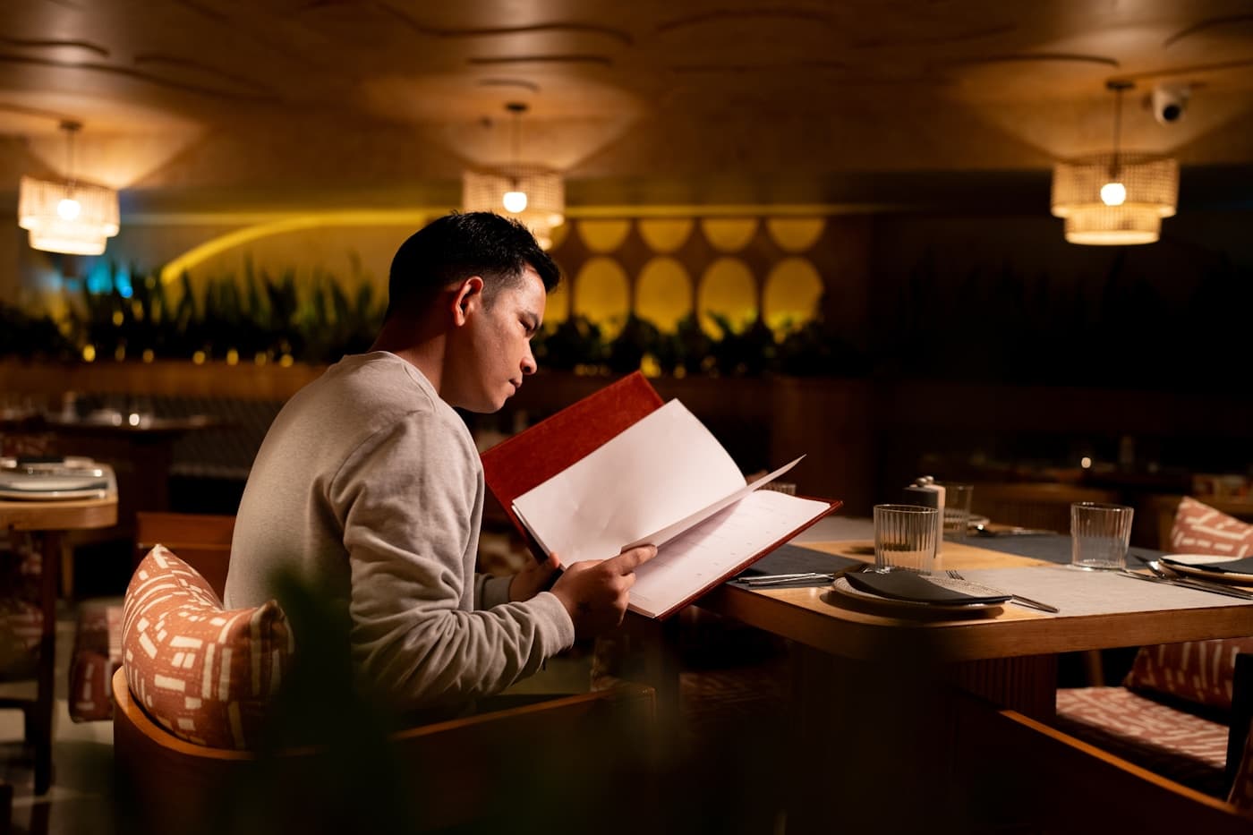 A person reading a menu at a warmly lit restaurant table.